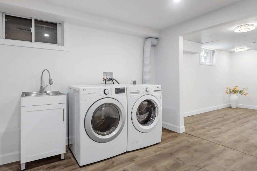 white washer and dryer machine on a white walled room with a sink at the left